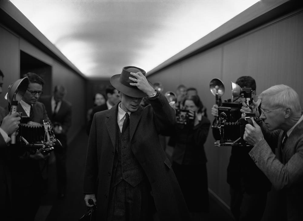 Fotograma en blanco y negro de Oppenheimer, con Cillian Murphy atravesando un pasillo lleno de periodistas (Universal Pictures)